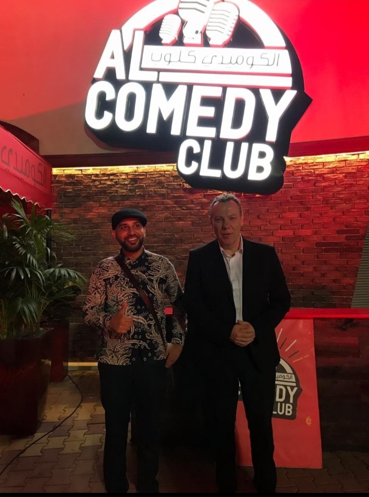 Mohsin Tutla giving a thumbs up beside a guest under the Al Comedy Club sign