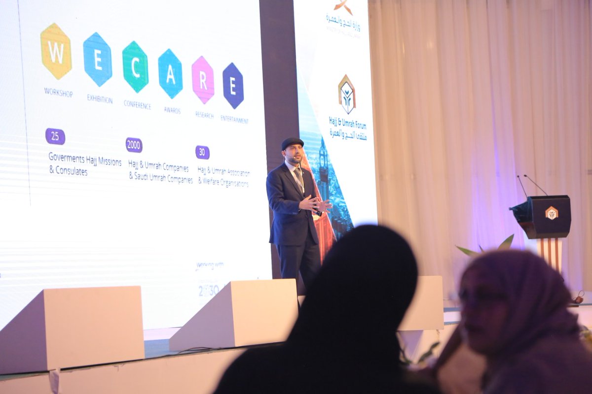 Mohsin Tutla on stage in front of a slide reading WE CARE: Workshop, Exhibition, Conference, Awards, Research, Entertainment