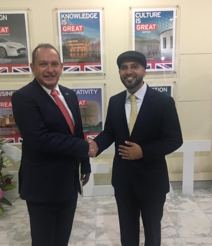 Mohsin Tutla shaking hands with a man beneath GREAT Britain campaign posters
