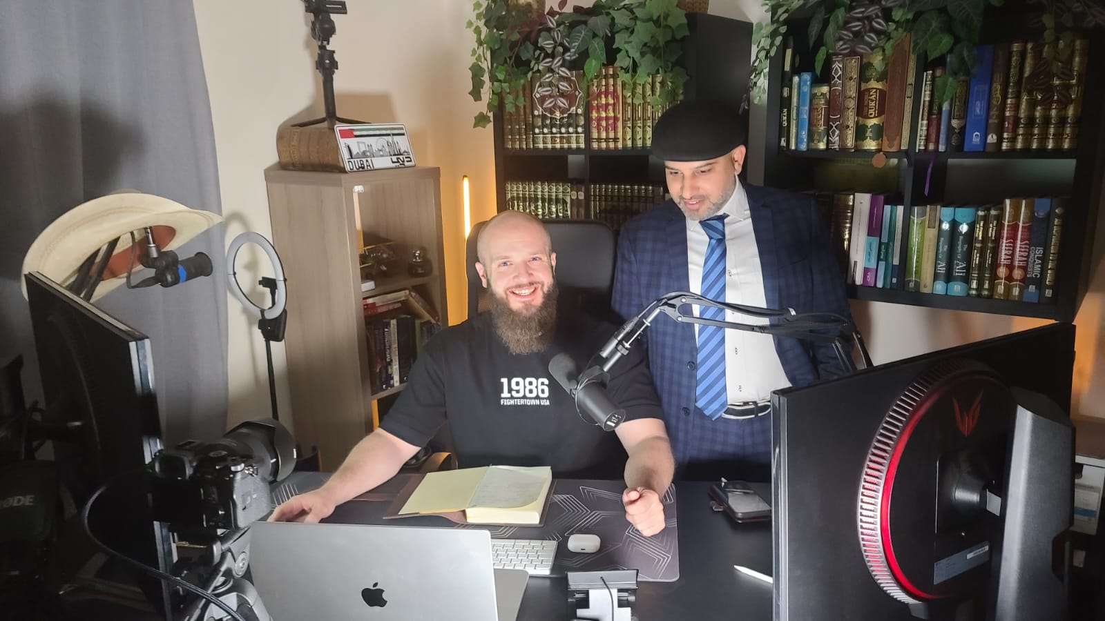 Mohsin Tutla standing beside a host at a podcast desk with a microphone and bookshelves
