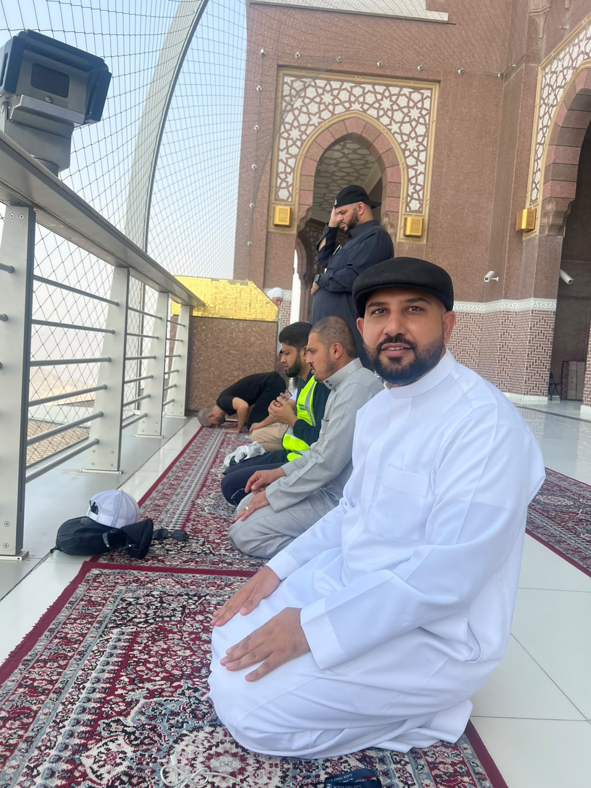 Mohsin Tutla seated on a prayer rug on the Clock Tower balcony with other worshippers